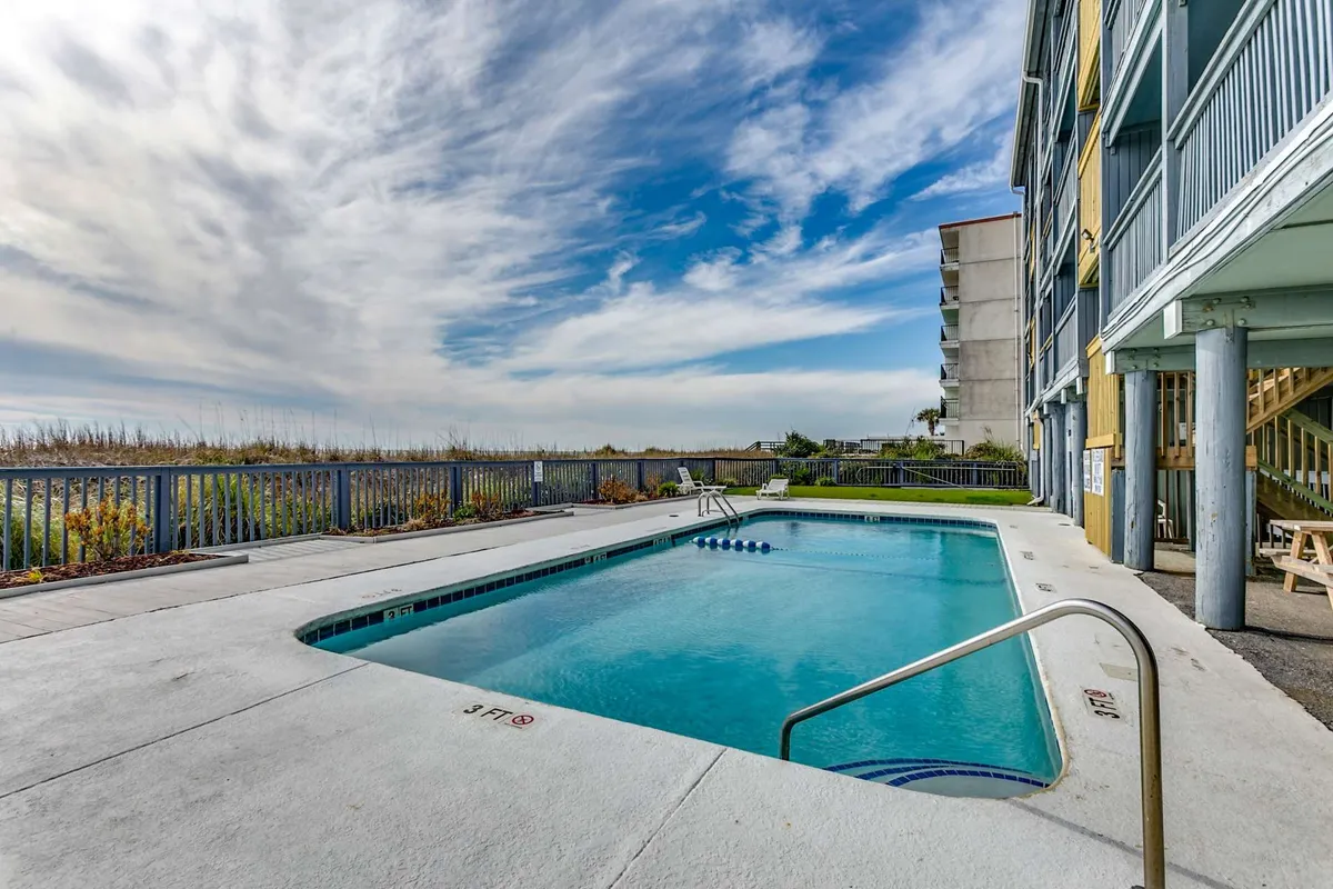 This exterior view showcases a swimming pool surrounded by the building structure and lush landscape, exuding an inviting and communal atmosphere. The setting is ideal for group activities like swimming, sunbathing, or family barbecues.