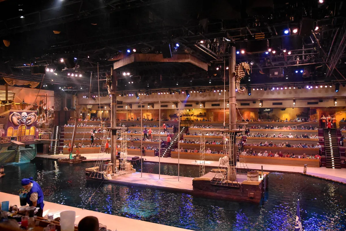 This interior image showcases a vibrant arena with a pirate-themed stage, water features, and audience seating, evoking the thrill of live entertainment experiences. The scene is buzzing with anticipation, capturing a group-friendly setting ideal for shared adventures and memorable nights out.