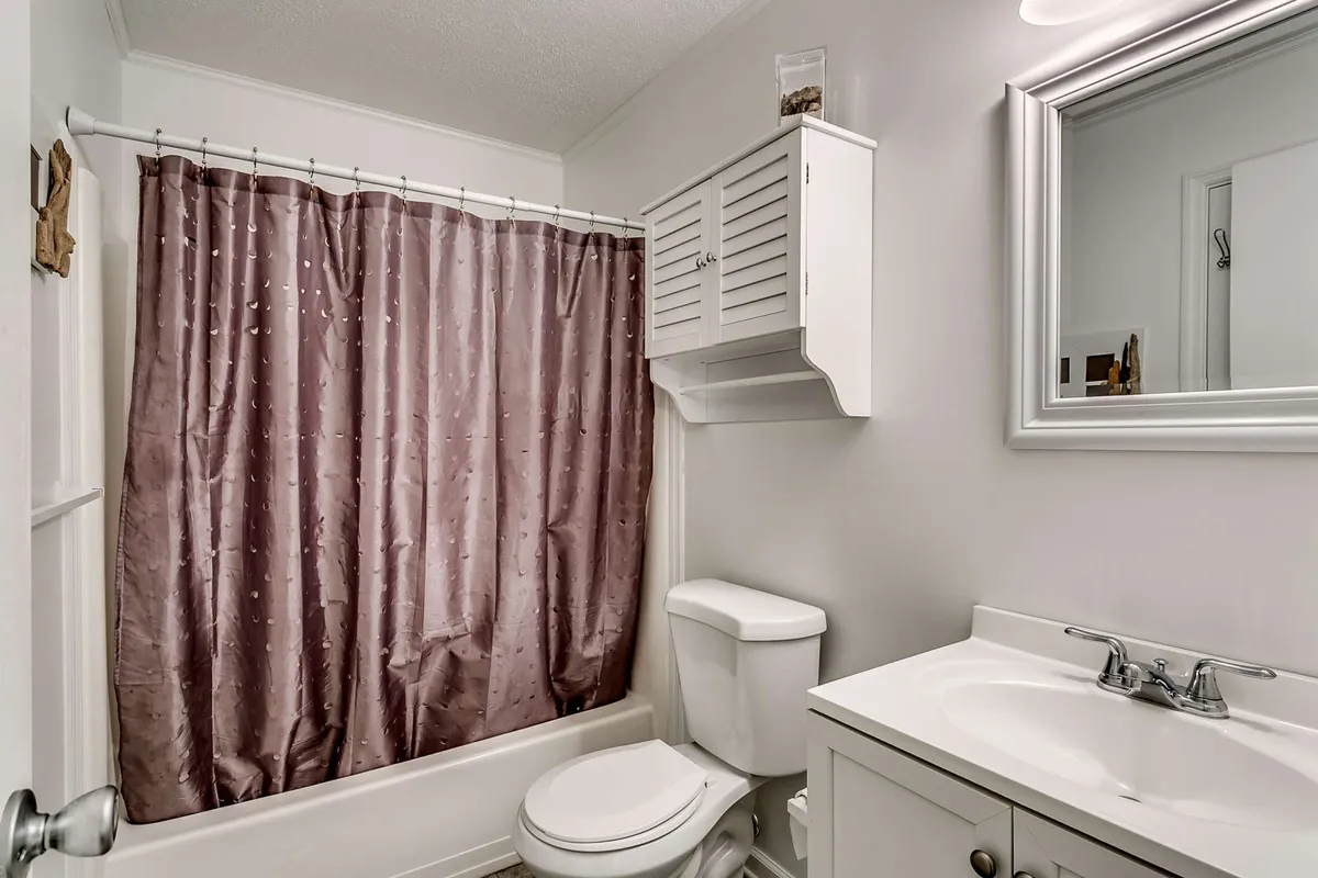 A bright, well-appointed bathroom featuring a shower curtain, vanity, and mirror. The space is neat and welcoming, suitable for morning routines or relaxing after a day at the beach.