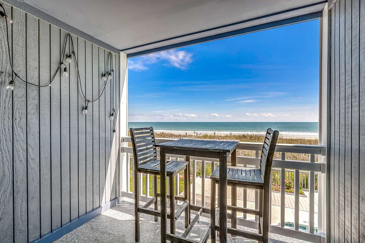 A serene private balcony with a wooden bar table and stools facing a breathtaking ocean view. The setup invites guests to enjoy their coffee at sunrise, cocktails at sunset, or simply watch the waves together in peace.