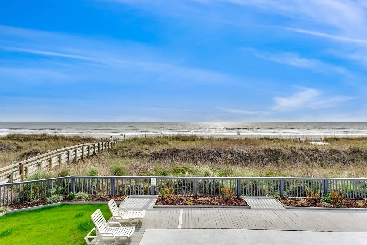This image showcases a serene beachfront view with lounge chairs set up along a wooden pathway that leads directly to the sandy shore. The calm ocean is visible in the background, and the scene exudes a relaxed, family-friendly atmosphere ideal for sunbathing, playing in the sand, and enjoying ocean views.