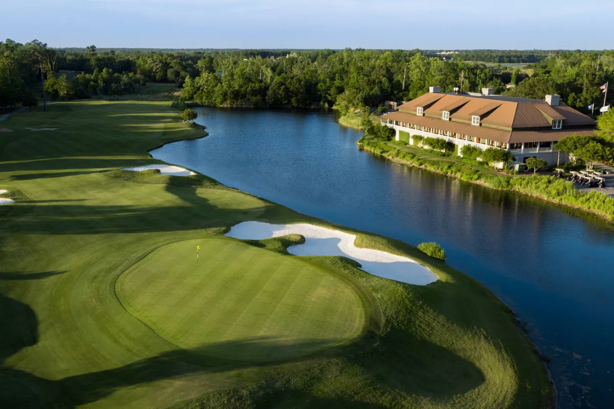 An expansive view of a lush golf course with a water feature, sand traps, and a clubhouse set amid well-maintained greenery. The scene is upscale and serene, suggesting both recreation and relaxation in an attractive outdoor setting.