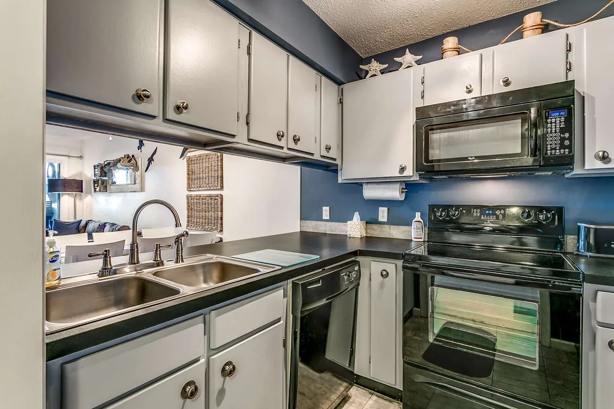 A contemporary kitchen highlighted by sleek stainless steel appliances, striking black countertops, and a bold blue accent wall. Decorative items on shelves and a spacious counter invite culinary creativity and social gatherings, matching the resort-style escape described in the section.